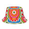 Reversible all-over print unisex bucket hat featuring two distinct bold designs. Side one showcases a psychedelic wavy stripe pattern in deep red, orange, green, blue, cream, and blush. Side two features a retro 70s groovy floral medallion print with large daisy motifs, red petals, yellow centers, and concentric pink, orange, and green rings on a cream background. Made from 100% polyester with a soft linen-feel texture. Moisture-wicking and breathable. Unisex sizing: XS/S and M/L/XL.
