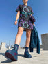 Cotton t-shirt dressA short-sleeve structured t-shirt dress with a black background. The dress features a bold, vertically stacked repeating graphic print. The design includes intricate damask patterns in teal and grey, purple roses with teal leaves, and a central evil eye motif set inside an ornate frame with small four-point stars. The heavyweight fabric holds a clean, straight cut above the knee with zero drape, maintaining a sculptural, slightly boxy silhouette.