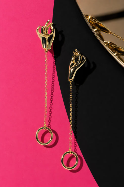 a pair of gold earrings with a unique design, hanging from chains against a contrasting background.