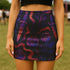 High-waisted mini skirt with dark botanical print featuring violet roses, fiery orange daggers, and swirling ribbon-like accents on a black background. Form-fitting silhouette with stretch eco-poly fabric and elastic waistband. Available in metallic glitter or smooth finish. A bold look for gothic, witchy, or alternative festival fashion.