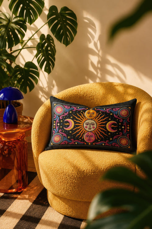 Rectangular 20x12 inch lumbar pillow cover in black featuring printed faux crewel embroidery of a large orange sunburst with a cream face, flanked by pink and yellow crescent moons, a golden moon face above and a pink moon face below, gold stars, blue dots, magenta and blue baroque scroll flourishes, and four corner medallions with golden flowers. Whimsigoth celestial design printed on both sides with a hidden zipper, crafted from soft linen look polyester.