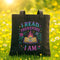 A black tote bag with a colorful graphic design on it, featuring a book, flowers, and stars, along with the text "I READ THEREFORE I AM" printed on it.