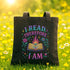 A black tote bag with a colorful graphic design on it, featuring a book, flowers, and stars, along with the text "I READ THEREFORE I AM" printed on it.