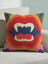 A colorful throw pillow with a graphic design of a pair of open, fanged mouths in red, blue, and yellow colors.