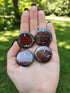 A collection of four glossy black circular pinback buttons featuring striking red and white gothic illustrations. One button shows "Midnight Graveyard Society" text with bats and tombstones. Another reads "Cemetery Picnic Society" with a coffin and umbrella icon. A third features a detailed white skull and red roses with "Memento Mori" text below. The final pin displays "Nocturnal Flower Society" surrounded by floral vines.