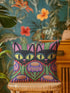 A square decorative pillow cover featuring a vibrant, symmetrical flat printed design that mimics the look of textured embroidery. Two black cats with large yellow eyes and pink noses face forward against a bright red background. Below the cats are large purple and pink flowers with green stems. Above the cats are green cactus shapes. The artwork uses bold, colorful outlines to create an optical illusion of stitching, though the fabric itself is smooth.