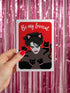 A vertical greeting card featuring a flat vector illustration of Robert Smith from The Cure against a vibrant red background. He has messy black hair, pale skin with smeared lipstick, and wears black cat ears. He is surrounded by four black cats with pink collars. White script text at the top reads "Be my Lovecat." The card is printed on shimmery pearlescent cardstock that catches the light. A high-quality alternative Valentine or anniversary card for goth music lovers and post-punk fans.