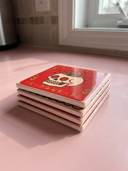 Set of four square glazed ceramic coasters featuring a vibrant pastel goth and creepy cute design. These functional art pieces show a spooky yet playful aesthetic perfect for alternative home decor. The coasters have a glossy wipe-clean finish and a non-slip cork backing to protect furniture surfaces from hot and cold beverages. Ideal for maximalist coffee tables, witchy desks, or as a unique housewarming gift for horror fans who love retro 70s and dopamine decor styles.