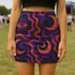A woman wearing a short skirt with a colorful, abstract pattern of swirls and lines in shades of purple, orange, and pink.