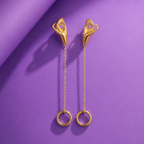 A pair of gold earrings with a chain and circular rings, displayed against a purple background.