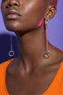 A close-up of a person's face wearing a pair of silver earrings with circular designs hanging from the earlobes.