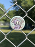 Round pinback button featuring a pastel mint green background with a cartoon grim reaper character in a lavender hood holding a protest sign. The design includes bold black outlined lettering reading “Pacifist Reaper” above the figure and small sparkle accents surrounding it. The finish is glossy and smooth, with a printed illustration style on a metal pin badge surface.