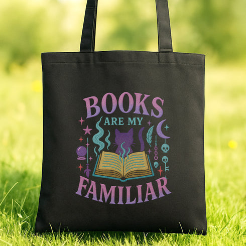 A black tote bag with a colorful graphic design on it, featuring the text "BOOKS ARE MY FAMILIAR" and various symbols related to books and reading.