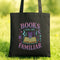 A black tote bag with a colorful graphic design on it, featuring the text "BOOKS ARE MY FAMILIAR" and various symbols related to books and reading.