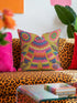 A square faux embroidery pillow featuring a brightly colored maximalist design against a mustard yellow background. In the center stands a stylized, furry Bigfoot or Sasquatch figure rendered in vibrant layers of pink, orange, blue, and lime green with a blue face and yellow eyes. The central creature is surrounded by large, detailed symmetrical pink and blue flowers and leaves. The flat printed fabric creates a highly realistic optical illusion of dimensional crewel embroidery stitches.