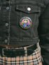 A round glossy metal pinback button featuring a flat 2D print illustration of an opossum wearing a blue cloak and a green crown. The opossum holds a neon green goblet in one paw and two purple dice in the other. A bright pink circle sits behind the opossum, surrounded by a black outer ring. Purple text reads PATRON SAINT OF BAD DECISIONS curved around the edge. Two pink roses with green leaves are on the sides. The design uses bold black outlines and bright neon colors.