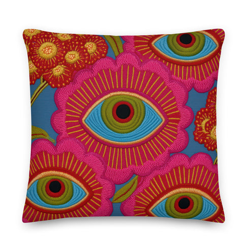 A square decorative throw pillow with a premium linen-feel texture. The design is a repeating pattern of stylized evil eyes on a dusty blue background. Each eye is rendered in turquoise, olive green, and black, and is framed by vibrant hot pink petals with radiating gold lines, resembling a flower or sunburst. The all-over print is colorful and has a visual texture that mimics embroidery. The pillow has a clean, knife-edge finish and a double-sided design, showcasing a bold, psychedelic pattern.