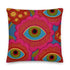 A square decorative throw pillow with a premium linen-feel texture. The design is a repeating pattern of stylized evil eyes on a dusty blue background. Each eye is rendered in turquoise, olive green, and black, and is framed by vibrant hot pink petals with radiating gold lines, resembling a flower or sunburst. The all-over print is colorful and has a visual texture that mimics embroidery. The pillow has a clean, knife-edge finish and a double-sided design, showcasing a bold, psychedelic pattern.
