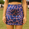 Bold high-waisted mini skirt with abstract blue giraffe spots on a pink background, perfect for festival fits and alt style lovers. Available in metallic or performance knit finishes. Sizes XS to XL.