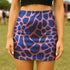 Bold high-waisted mini skirt with abstract blue giraffe spots on a pink background, perfect for festival fits and alt style lovers. Available in metallic or performance knit finishes. Sizes XS to XL.