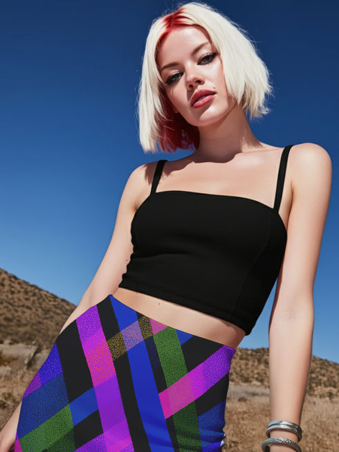 A young woman with blonde hair and red highlights is posing in a desert-like setting, wearing a black crop top and a colorful, patterned skirt.