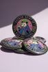 A round glossy metal pinback button featuring a flat 2D print illustration of an opossum wearing a blue cloak and a green crown. The opossum holds a neon green goblet in one paw and two purple dice in the other. A bright pink circle sits behind the opossum, surrounded by a black outer ring. Purple text reads PATRON SAINT OF BAD DECISIONS curved around the edge. Two pink roses with green leaves are on the sides. The design uses bold black outlines and bright neon colors.