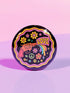 Round pinback button badge with a black background, featuring a retro illustration of a red revolver shooting out a rainbow flag that says “LOVE.” Surrounded by colorful 70s-style flowers and peace signs, outlined in wavy neon border. Glossy finish with vibrant pop colors and psychedelic design.