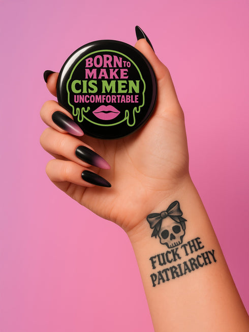 Glossy black pinback button featuring bold text 'Born to Make Cis Men Uncomfortable' in pink and green glitter fonts. Design includes melting skull outline and lips illustration. Button is round and 2.25 inches in diameter with a durable tinplate body and UV-resistant coating. Perfect for jackets, backpacks, or gifts for queer punks and feminists.