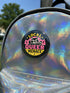 Round pinback button badge with Local Queer Menace text in bold yellow and pink retro lettering on a black background. A cartoon raccoon with a spiked collar flips the middle finger with a painted pink nail, framed by a hot pink sunburst, lightning bolts, and star accents. Glossy laminate finish over durable metal tinplate with a secure safety pin backing. Funny queer pride pin available in 2.25 inch and 3 inch sizes for jackets, totes, lanyards, and backpacks.