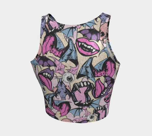 A sleeveless cropped tank top made from stretchy performance knit fabric. The all-over print features a dense, scattered pattern of pastel goth and creepy cute motifs over a light background. Graphics include pink and blue bats in flight, floating eyeballs with blue irises, pink skulls, and glossy vampire lips with sharp white fangs and tongues sticking out. The neckline is a high scoop and the armholes are curved. The fabric comes in either a matte finish or a sparkly silver glitter foil.