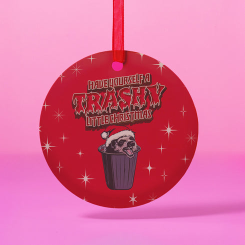 Round red metal Christmas ornament featuring angry possum in Santa hat emerging from trash can. Text reads "Have Yourself a Trashy Little Christmas" in dripping font with stars.