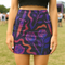 High-waisted mini skirt with dark botanical print featuring violet roses, fiery orange daggers, and swirling ribbon-like accents on a black background. Form-fitting silhouette with stretch eco-poly fabric and elastic waistband. Available in metallic glitter or smooth finish. A bold look for gothic, witchy, or alternative festival fashion.