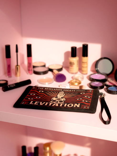 A rectangular makeup bag featuring a vibrant psychedelic print with gothic elements. The fabric texture is clearly visible showing a woven linen-like polyester grain. A black zipper runs across the top edge with a black detachable nylon wrist strap clip on the side, showcasing the approximately nine by six inch dimensions. The print includes high contrast neon colors and trippy swirling patterns typical of maximalist decor.