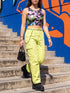 A close-up view of a sleeveless performance knit crop top featuring a vibrant pastel goth all-over print on a solid black background. The repeating pattern includes large black vampire bats flying over dripping, melted slime shapes in neon green. Wavy, warped checkerboard patterns in pastel pink, light purple, and black weave through the design. The graphic is finished with stylized, oversized pastel floral motifs and large open eyeballs staring outward.