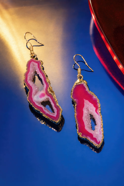 A pair of earrings with pink and red gemstone-like shapes, set against a blue background.