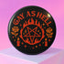 Round glossy pinback button measuring 2.25 inches with bold red graphic design on a black background. Text reads “Gay As Hell” above a red pentagram surrounded by flames, stars, roses, and candles. Made of tinplate with a safety pin back and a scratch-resistant mylar finish. The button features a high-gloss surface and is lightweight and durable, perfect for jackets, bags, or accessories.