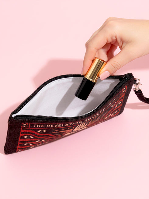 A rectangular makeup bag featuring a vibrant psychedelic print with gothic elements. The fabric texture is clearly visible showing a woven linen-like polyester grain. A black zipper runs across the top edge with a black detachable nylon wrist strap clip on the side, showcasing the approximately nine by six inch dimensions. The print includes high contrast neon colors and trippy swirling patterns typical of maximalist decor.