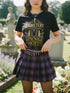 A black unisex crewneck graphic t-shirt featuring an ornate Victorian-inspired emblem printed on the chest in vintage gold and off-white. The centralized, symmetrical design showcases a classic coffin with a cross on the lid, flanked by wrought-iron cemetery gates. Beautiful scrollwork and decorative filigree flourishes surround the bold, retro serif text reading CEMETERY PICNIC SOCIETY. A crescent moon and stars sit at the top, completing this gothic memento mori graphic shirt.