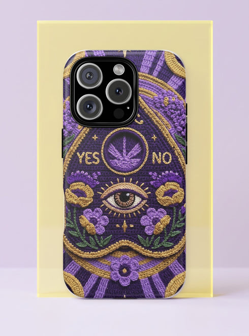 A matte finish phone case featuring a 2D optical illusion of a textured, purple crochet Ouija board planchette. The design includes intricate gold faux-embroidered borders, the words YES and NO, a central all-seeing eye, and a botanical leaf motif in the center circle. Lilac purple flowers and green leaves decorate the bottom half. The case has black rubber lining around the edges and camera cutouts. It looks like a thick, handmade yarn textile but is completely flat and smooth.