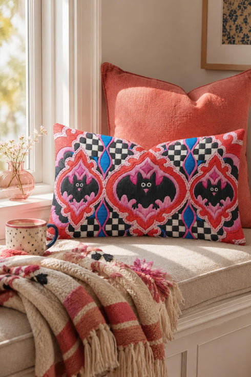 Rectangular 20x12 inch lumbar pillow cover in red featuring printed faux embroidery of three black bats with white eyes and pink noses, each framed in an ornate ogee medallion with pink flame stitch centers, black and white checkerboard accents, and cobalt blue diamonds. Whimsigoth damask bat design printed on both sides with a hidden zipper, crafted from soft linen look polyester for spooky maximalist home decor.