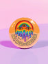 Round orange pinback button featuring bold rainbow psychedelic artwork of a melting third-eye face beneath a rainbow arch. Surrounded by stars and the phrase “Hot, Queer and Radiating” in retro black bubble letters. Glossy metal badge with UV-resistant mylar face and secure safety pin back.