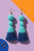 A pair of turquoise tassel earrings with gold hooks, displayed against a purple and orange background.