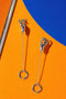 a pair of silver earrings with circular rings and dangling chains, set against a vibrant orange and blue background.