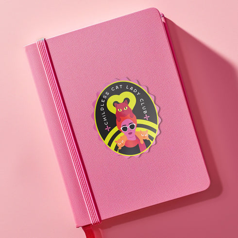Vibrant oval sticker reading "Childless Cat Lady Club". Features cartoon woman with sunglasses surrounded by cats. Bold retro design in pink, yellow, and red.
