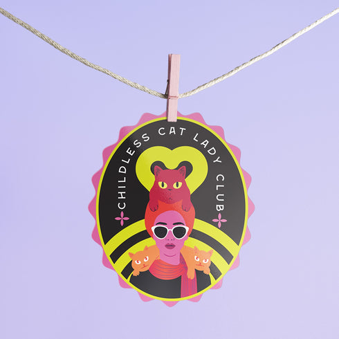 Vibrant oval sticker reading "Childless Cat Lady Club". Features cartoon woman with sunglasses surrounded by cats. Bold retro design in pink, yellow, and red.