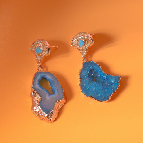 A pair of earrings featuring vibrant blue agate geode slices with natural crystal formations. Each earring has a 14k gold-plated fan-shaped post adorned with a small zircon rhinestone, combining earthy textures with Art Deco-inspired elegance.