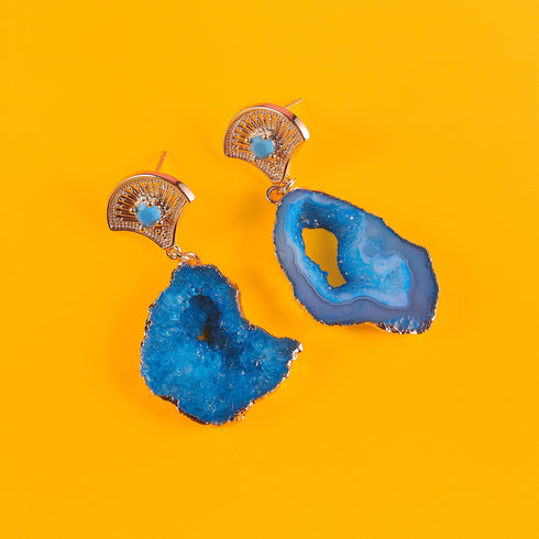 A pair of earrings featuring vibrant blue agate geode slices with natural crystal formations. Each earring has a 14k gold-plated fan-shaped post adorned with a small zircon rhinestone, combining earthy textures with Art Deco-inspired elegance.