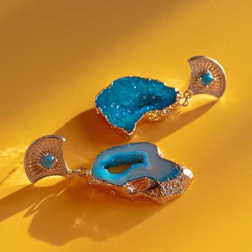 A pair of earrings featuring vibrant blue agate geode slices with natural crystal formations. Each earring has a 14k gold-plated fan-shaped post adorned with a small zircon rhinestone, combining earthy textures with Art Deco-inspired elegance.