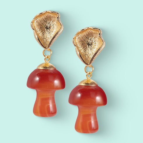 Handmade earrings featuring red agate mushroom-shaped drops with gold-plated caps, suspended from textured gold studs, showcasing unique cottagecore and boho aesthetic.