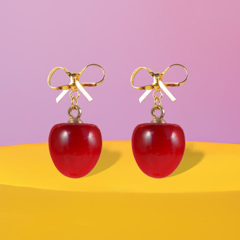 Gold bow earrings with dangling red cherry charms. Coquette-style jewelry perfect for soft girl and balletcore aesthetics. Handmade resin fruit earrings for summer style.